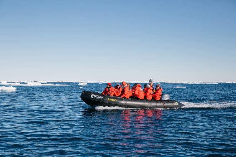 Ein Schlauchboot mit Gästen der Kreuzfahrt fährt durch ein Feld mit Eisschollen vor Spitzbergen